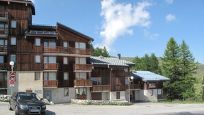 Un edificio de madera de varios pisos con balcones, un letrero que indica un restaurante y un automóvil estacionado al frente.