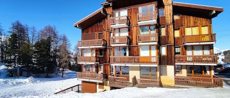 A multi-story wooden building with balconies, surrounded by snow and trees.