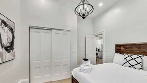 Un dormitorio con una cama, una araña, un armario y un cuadro en la pared.