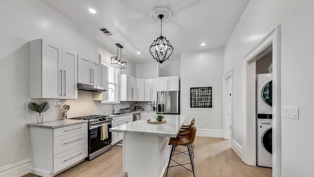 Una cocina moderna con armarios blancos, una isla central, un candelabro y una lavadora al fondo.