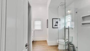 A modern bathroom with a glass shower enclosure, a white toilet, and a framed picture on the wall.