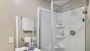 Een moderne badkamer met een douchecabine van glas, een wit wastafelmeubel met spiegel, en een handdoek aan de muur.