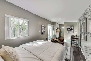 Une chambre avec un grand lit, un bureau et une chaise. On y trouve des fenêtres, un radiateur et un miroir.