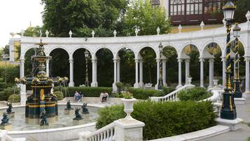 A classical garden with a fountain, white columns, and ornate lamp posts.