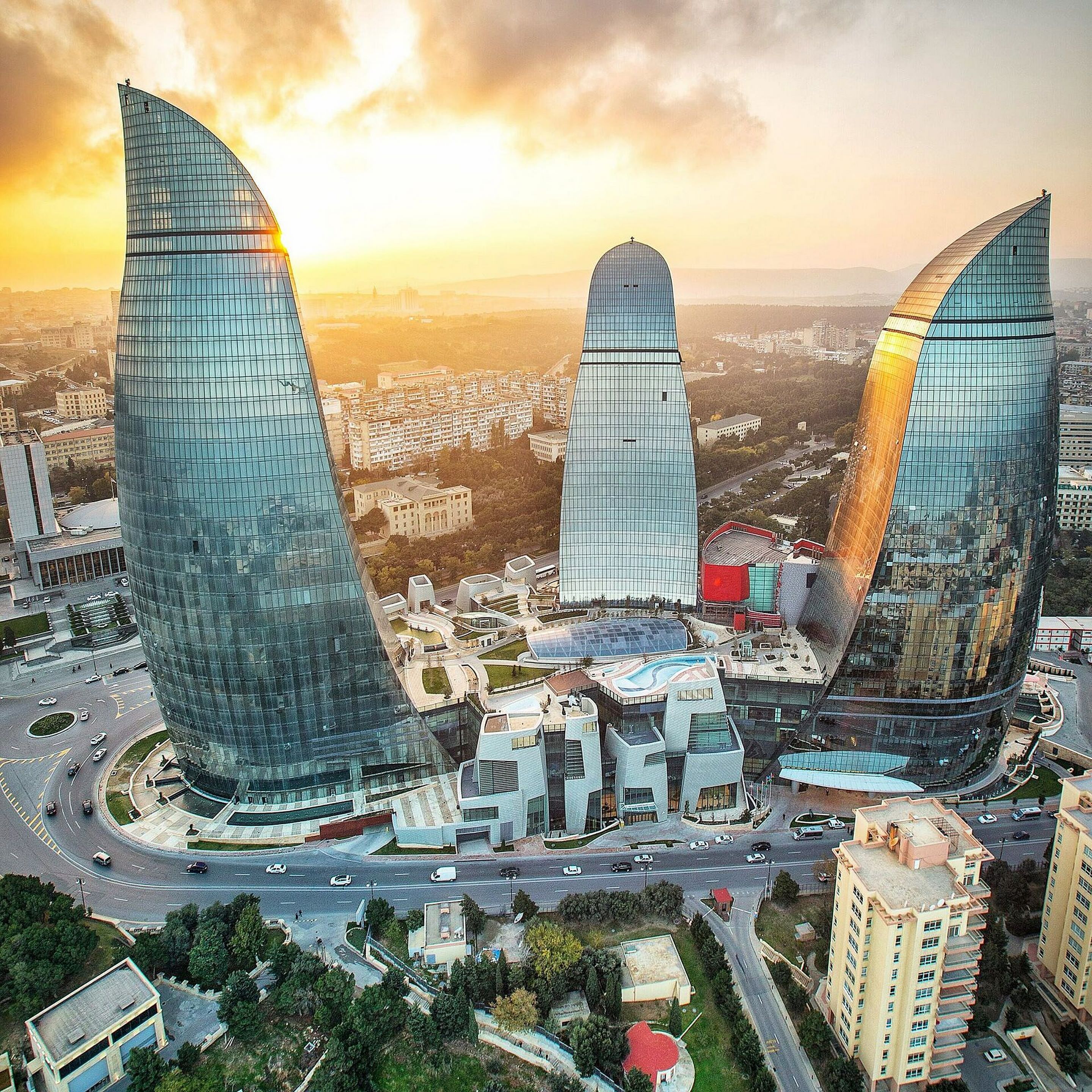 Un paysage urbain moderne, dominé par trois gratte-ciel imposants aux façades de verre incurvées, entourés d’un mélange de bâtiments résidentiels et commerciaux.