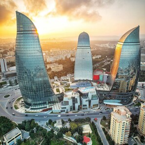 A modern urban landscape with three prominent skyscrapers featuring curved glass facades, surrounded by a mix of residential and commercial buildings. - Royal Sapphire Hotel (Baku)