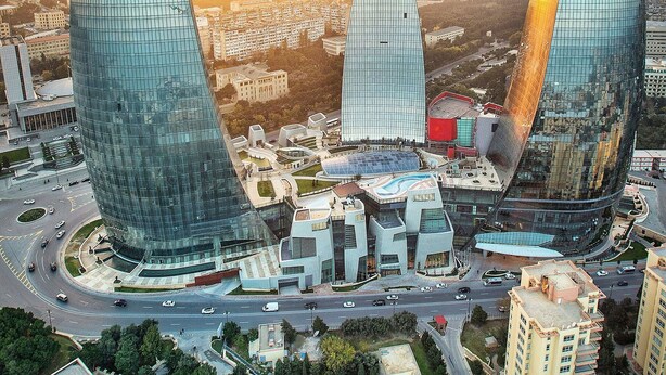 A modern urban area with three prominent skyscrapers featuring curved glass facades, surrounded by a mix of residential and commercial buildings. - Royal Sapphire Hotel (Baku)