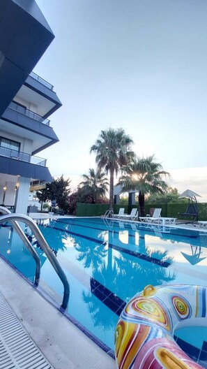 A swimming pool with lounge chairs and palm trees, surrounded by a modern building. - Palmila Butik Otel (Silifke)