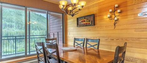 A dining area with a wooden table and chairs, a chandelier, and a painting on the wall.
