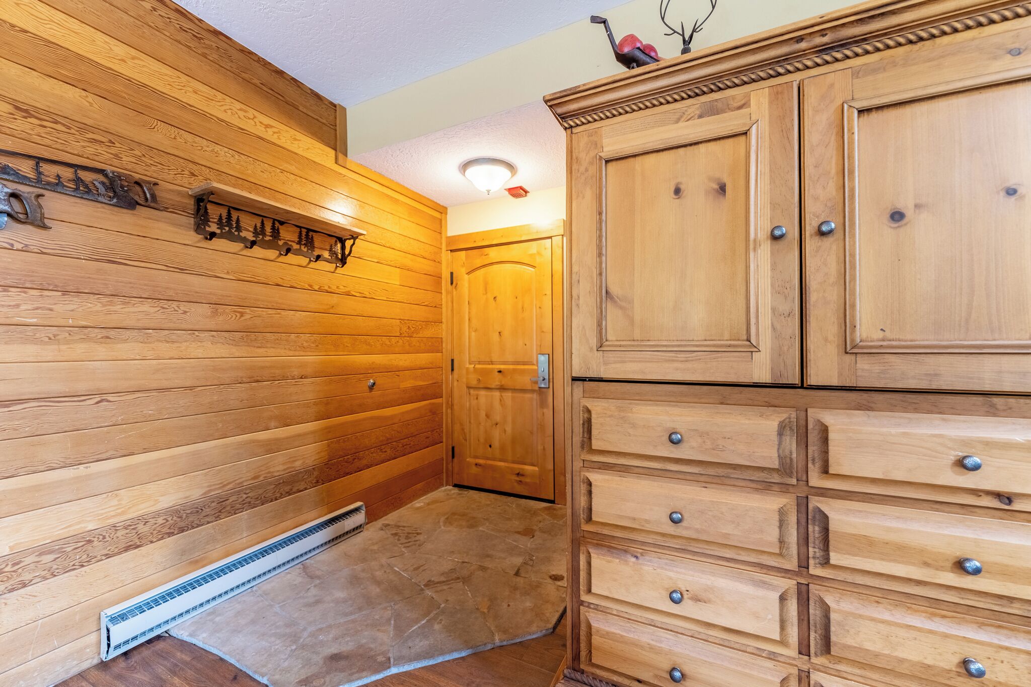 A wooden interior with a stone floor, a wooden cabinet with drawers, and a wooden door.