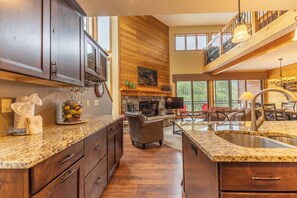 A spacious kitchen with granite countertops, wooden cabinets, and a stone fireplace.