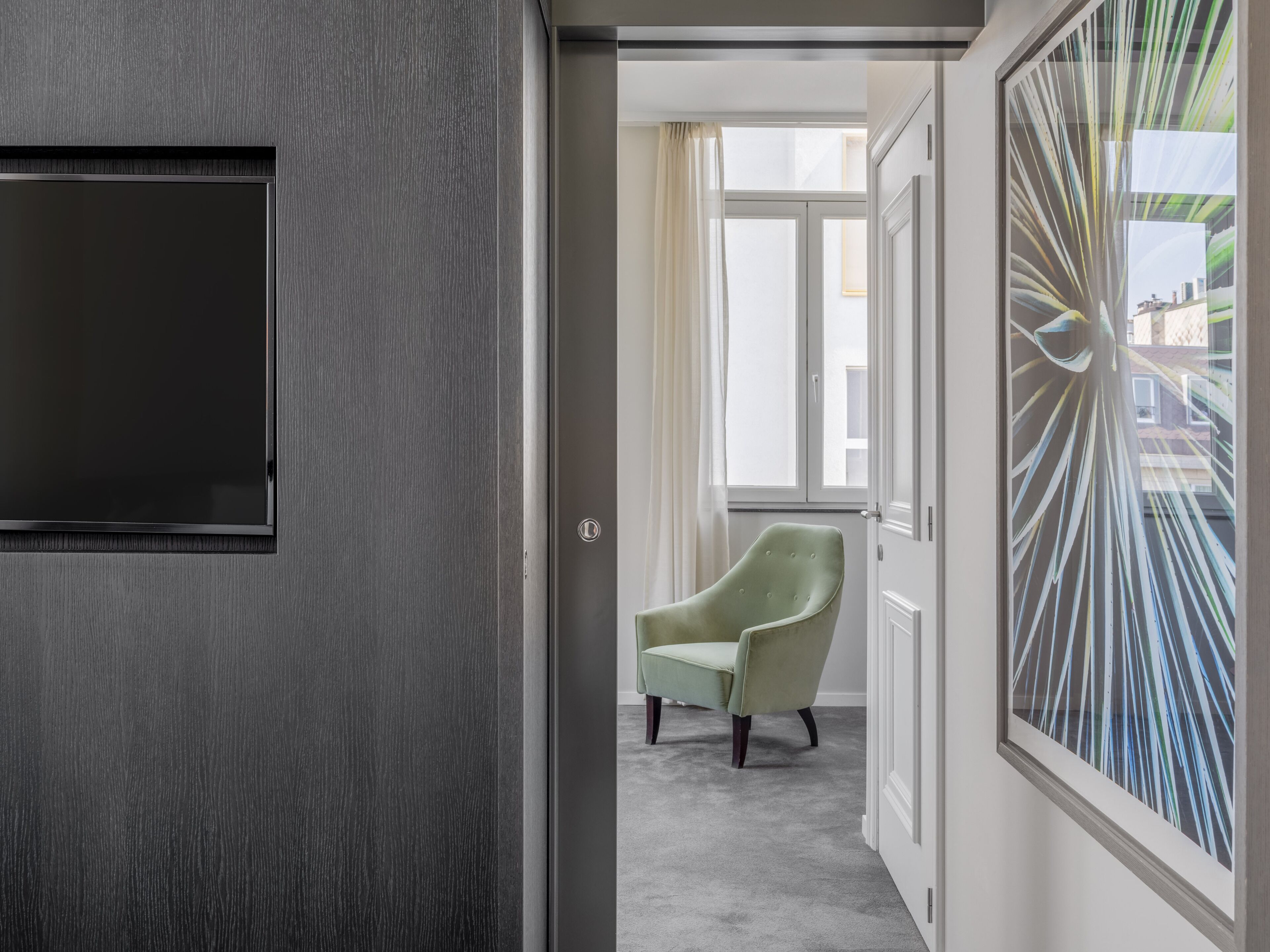 A hallway with a grey door, a green armchair, and a large abstract painting.