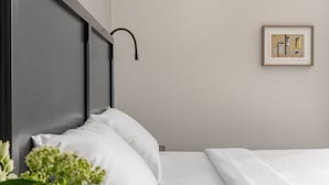 Un lit bien fait, avec du linge de lit blanc, une tête de lit sombre et un seul tableau encadré accroché au mur.