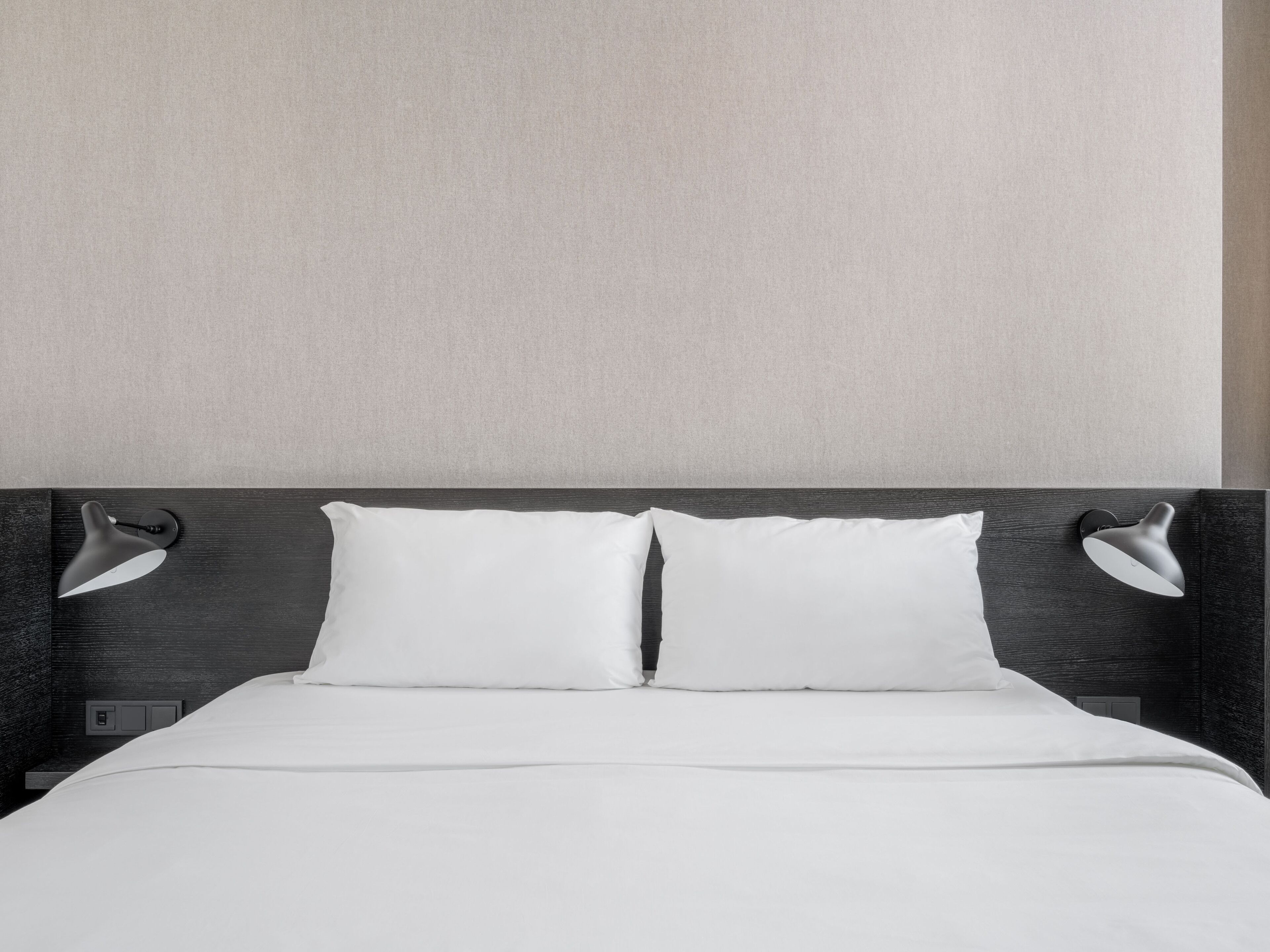 A neatly made bed with two pillows and two wall-mounted lamps on either side.