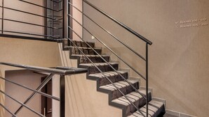 Un escalier moderne avec des rampes en métal et des marches recouvertes de moquette, menant à un palier doté d’une porte.