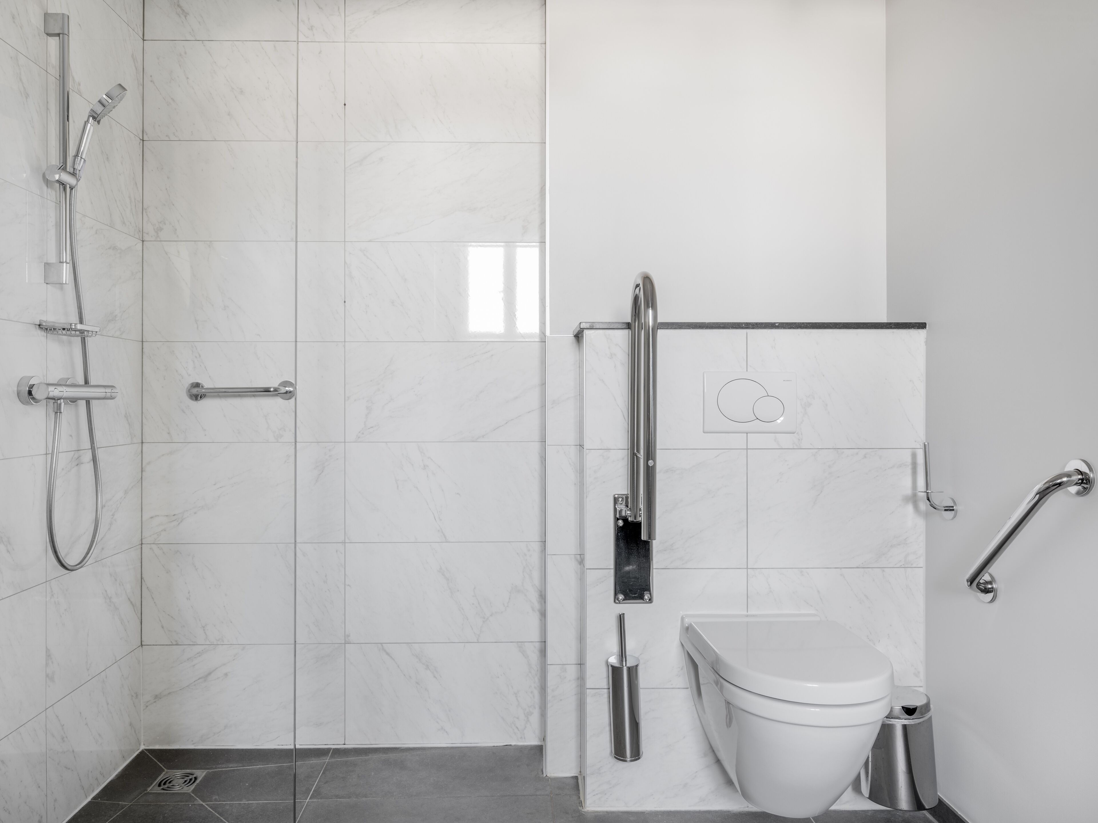 A modern bathroom with a shower, toilet, and grab bars.