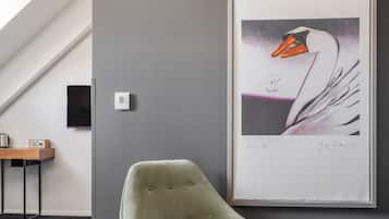 Una habitación moderna con pared gris, una obra de arte enmarcada de un cisne, un sillón verde, una mesita con un altavoz y un termostato.