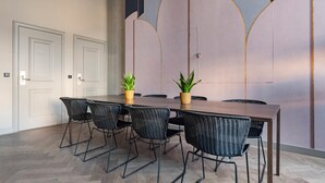 Une salle de conférence avec une longue table, des chaises en osier noir et deux plantes en pot.