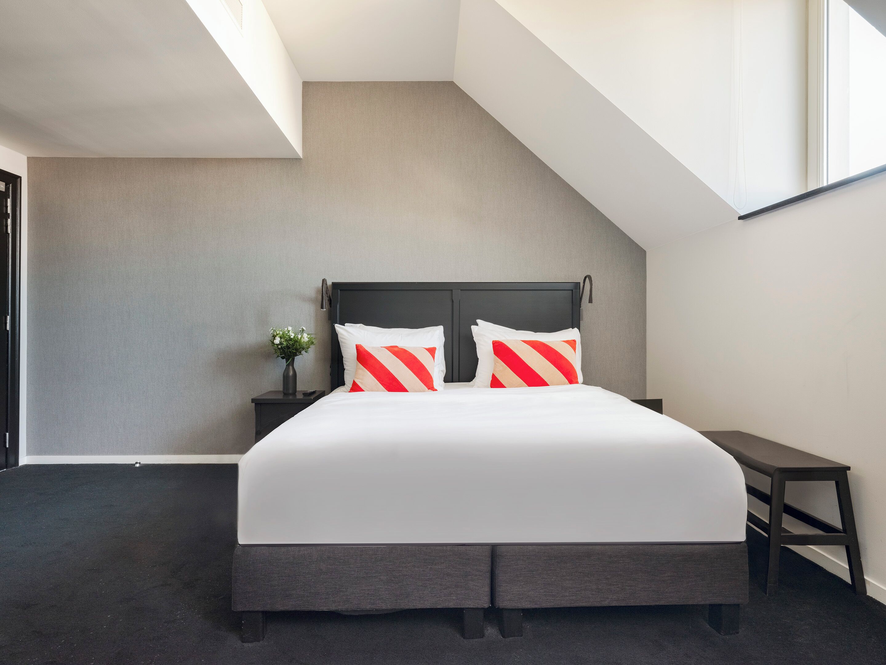 Een moderne slaapkamer met een groot bed, een nachtkastje, een klein tafeltje en een raam.
