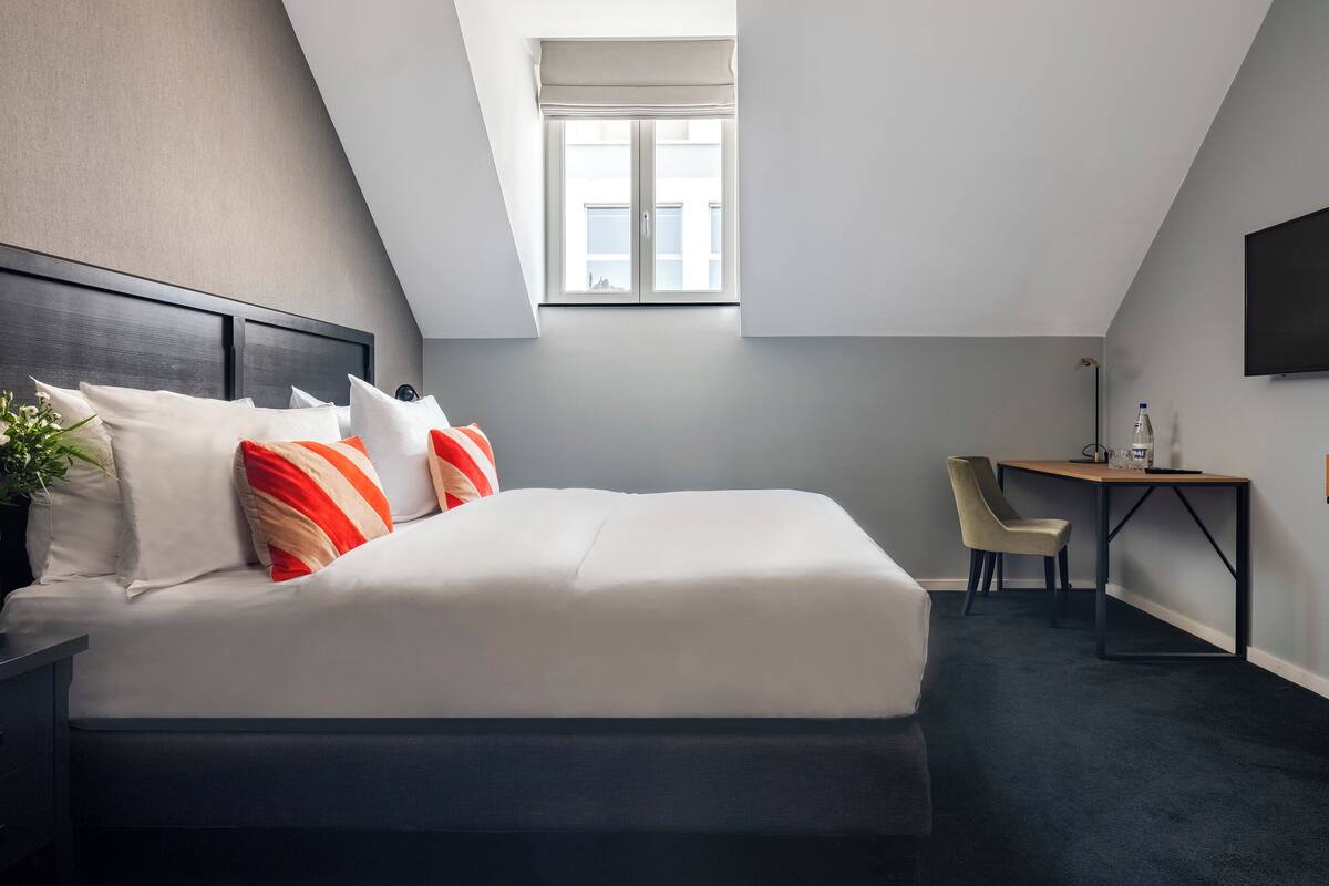 A modern hotel room with a neatly made bed, a desk, and a chair.