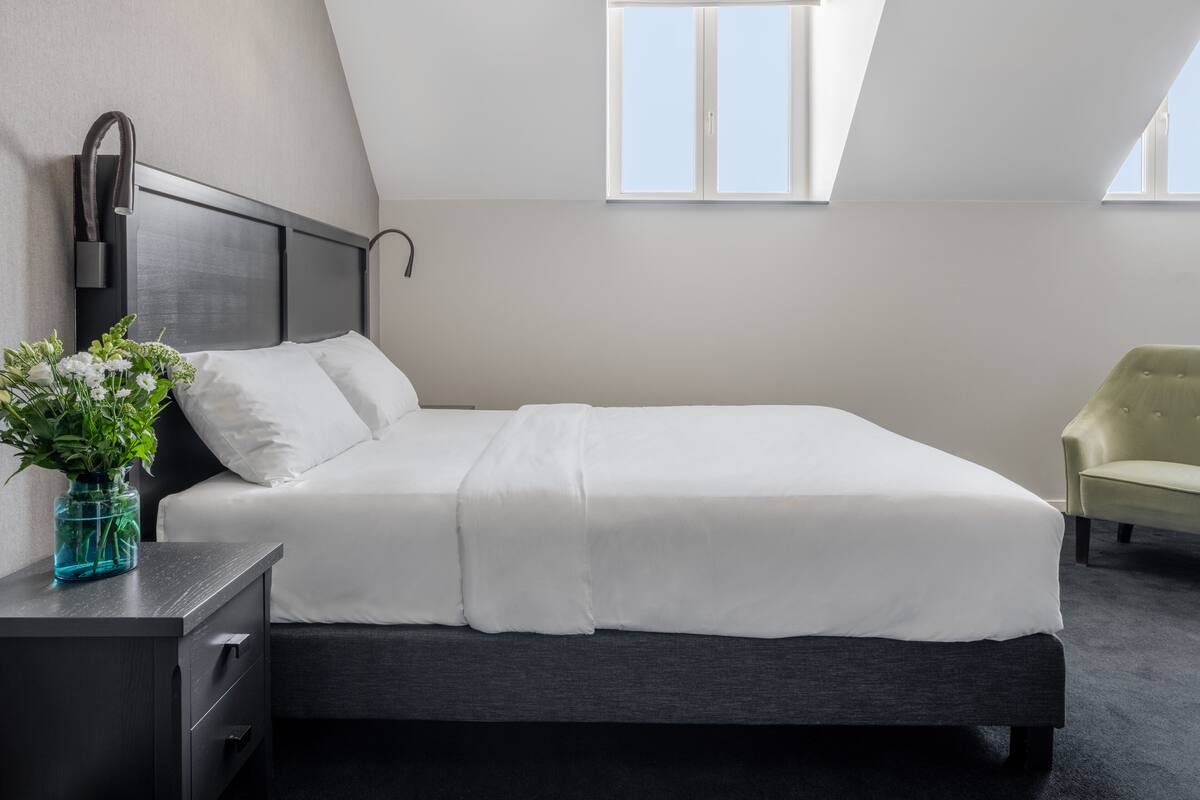 A modern hotel room with a bed, bedside table, and a chair.