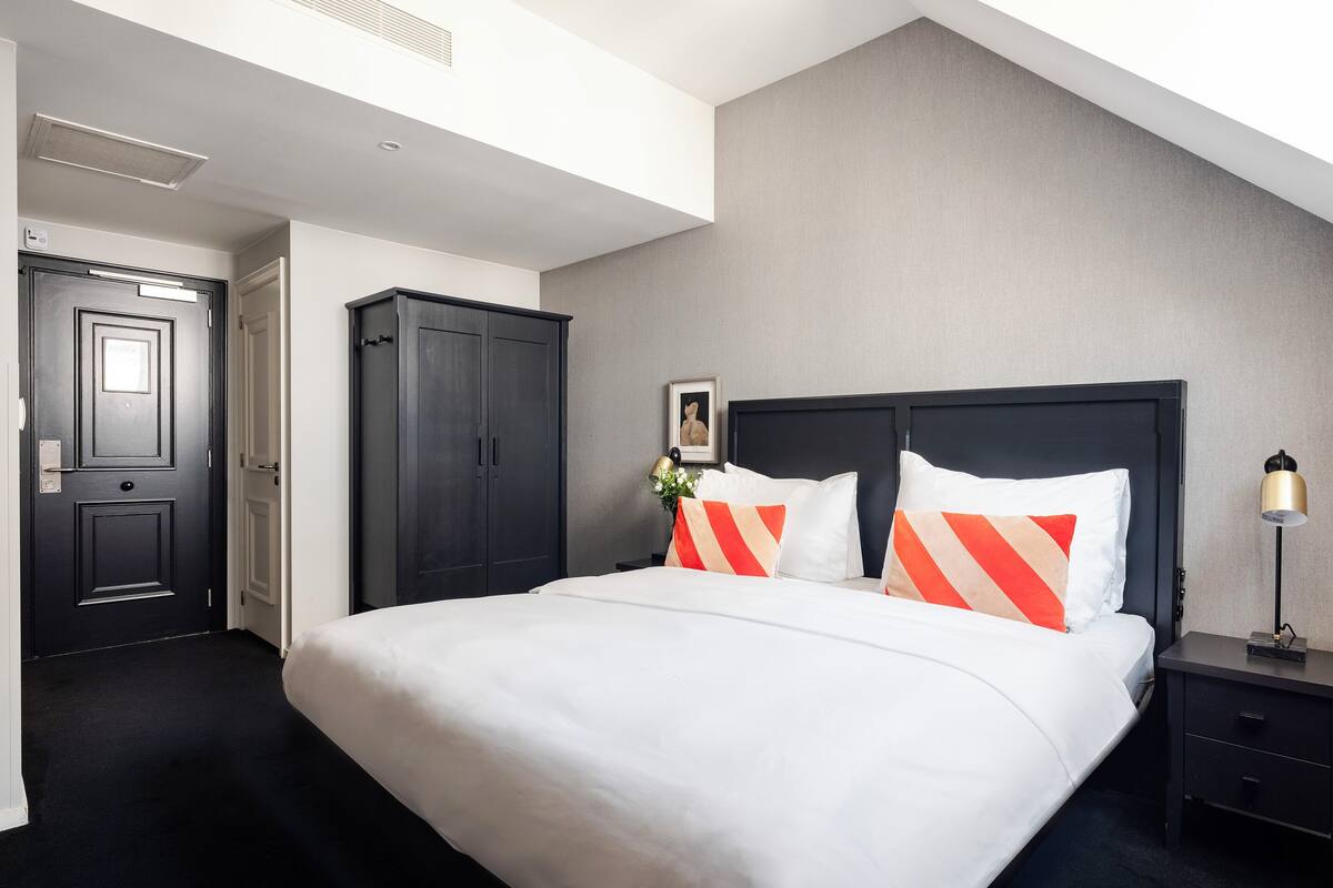 A hotel room with a large bed, a dark headboard, a nightstand, and a wardrobe.