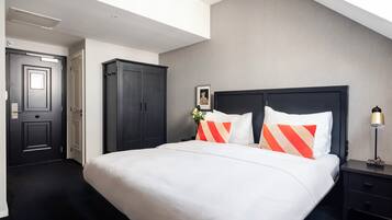Una habitación de hotel con una cama grande, cabecera oscura, mesita de noche y armario.