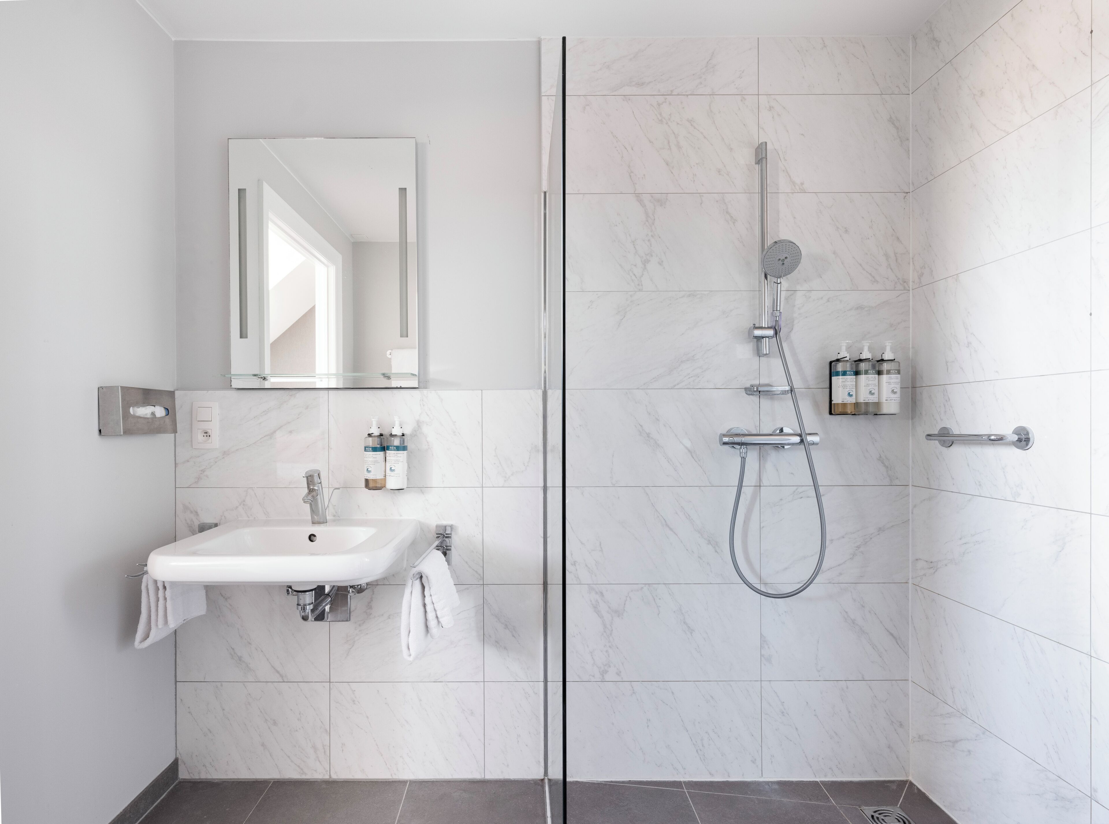 Un baño moderno con ducha de vidrio, lavamanos con toallero y espejo sobre el lavamanos.