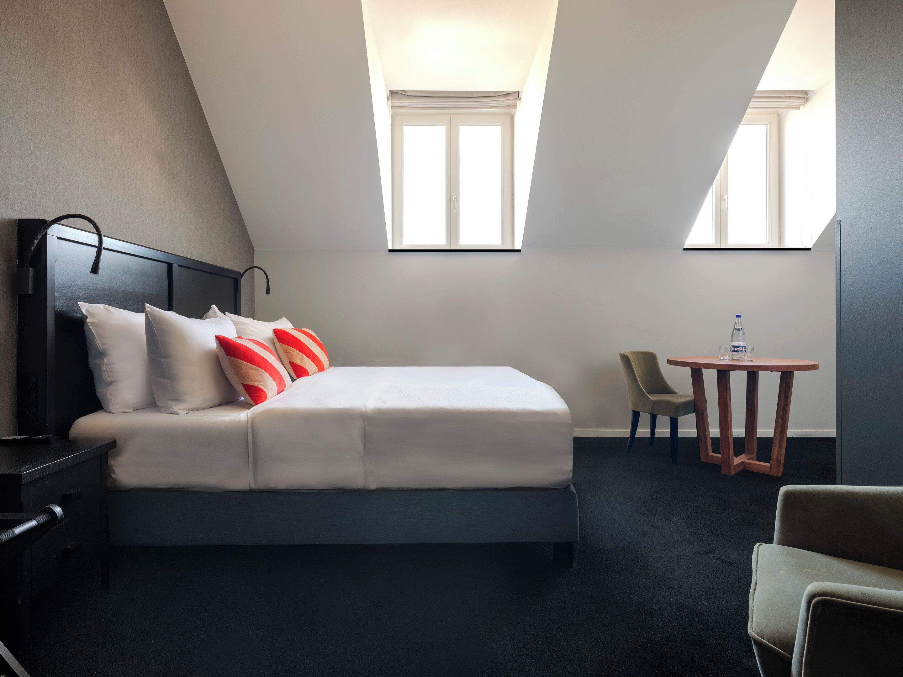 A hotel room with a bed, a desk, a chair, and two windows.