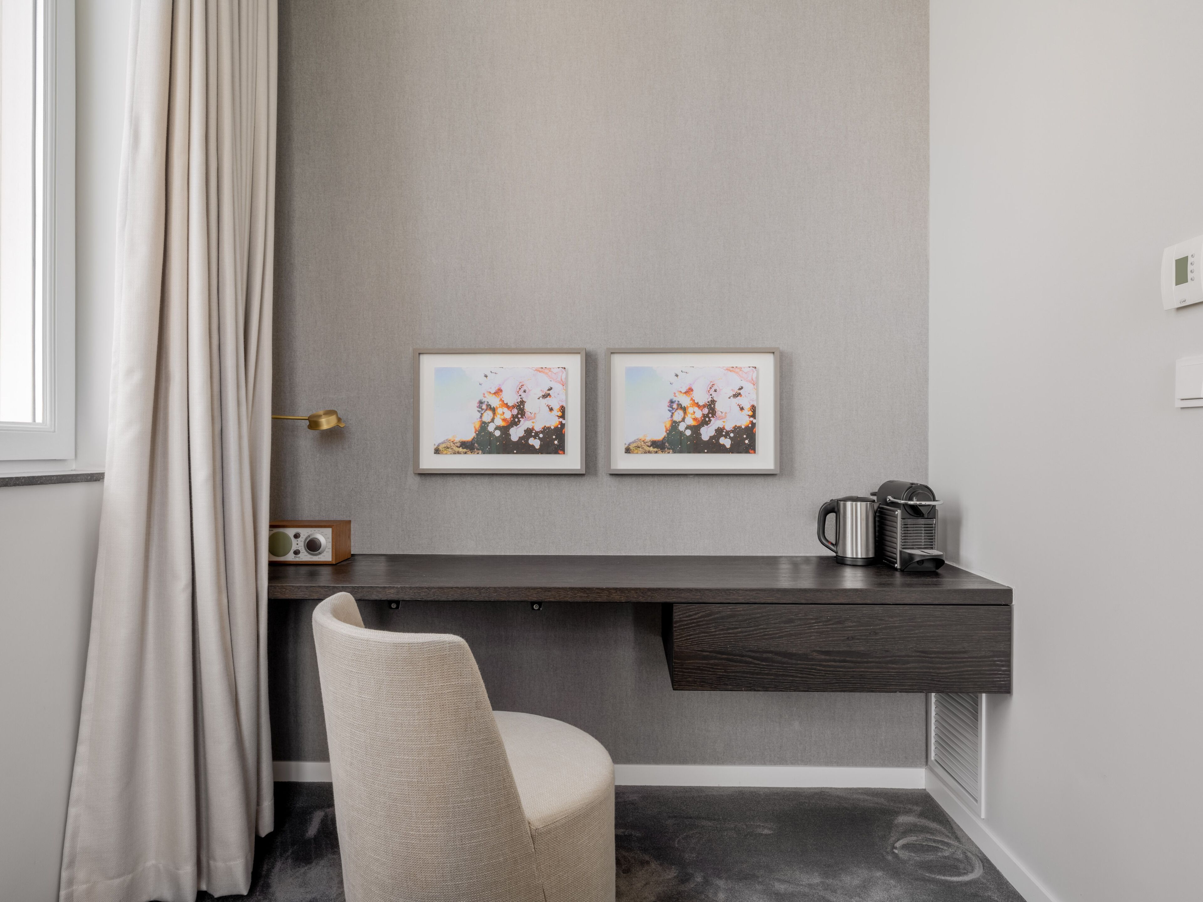 A modern room with a dark wooden desk, a beige chair, and two framed abstract paintings on the wall.