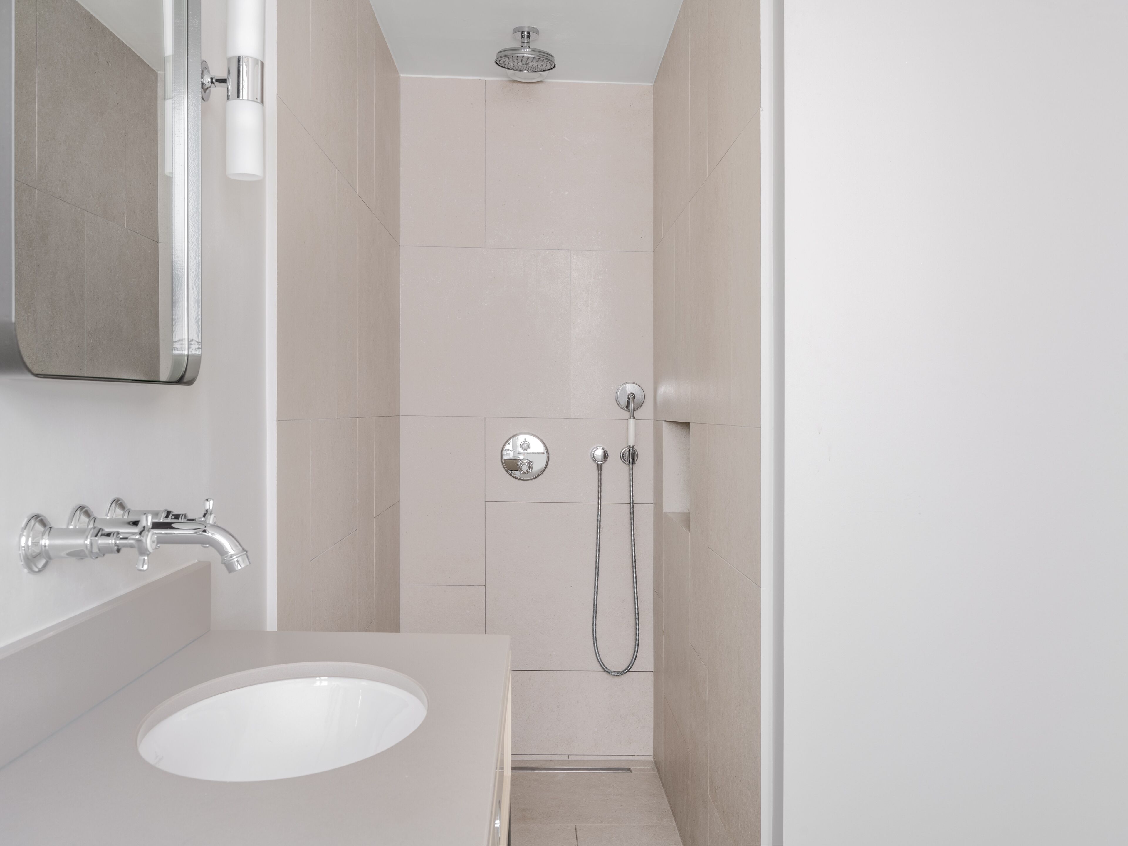 Une salle de bain moderne avec un lavabo blanc, un miroir, une douche équipée d’un pommeau de douche à main et un porte-serviettes.