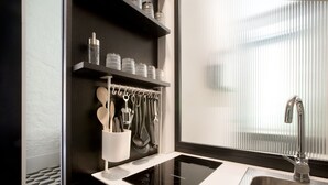 Una cocina moderna con encimera negra, pileta de acero inoxidable y ventana con persianas.