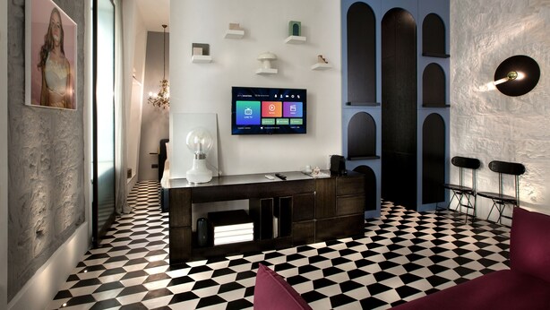 Una sala moderna con piso a cuadros, un televisor de pantalla plana montado en la pared, una consola de madera oscura y un sofá rojo.