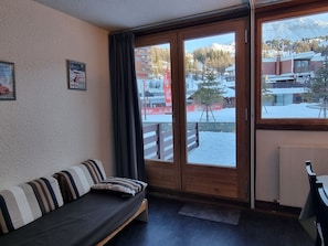A room with a sofa, a window with a view of a snowy mountain and buildings, and a radiator.