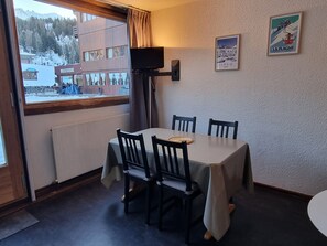 A dining area with a table and chairs, a window with a view of a snowy landscape, and a poster on the wall.