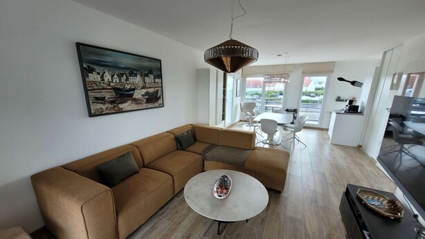 A modern living room with a brown sectional sofa, a round coffee table, and a dining area with white chairs.