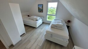A bedroom with two beds, a window with a view, and a painting on the wall.
