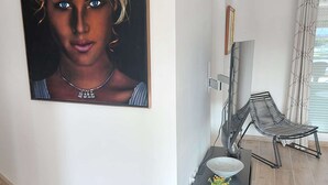 A modern interior with a framed artwork, a metal chair, a small table with a bowl and flowers, and a tiled floor.