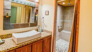 Un baño con techo de madera, un espejo grande, un lavamanos y una zona de ducha.