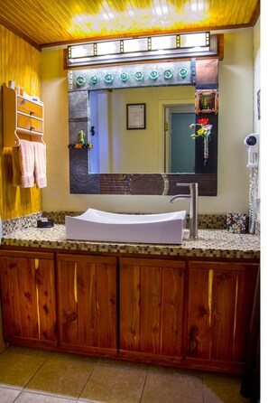 Un baño con tocador de madera, un lavabo blanco y un espejo encima.