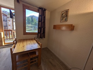 A wooden dining table with chairs, a window with a view of mountains, and a painting on the wall.