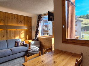 A cozy room with a wooden wall, a sofa, a wooden table, and a window with a view of buildings.