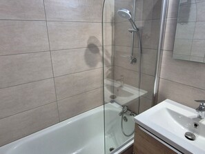 A bathroom with a glass-enclosed shower, a white sink, and a mirror.