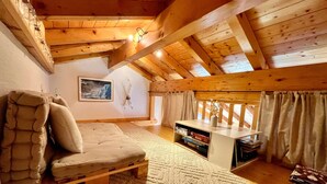 A cozy attic room with a loft bed, a small wooden table with books, and a window with curtains.