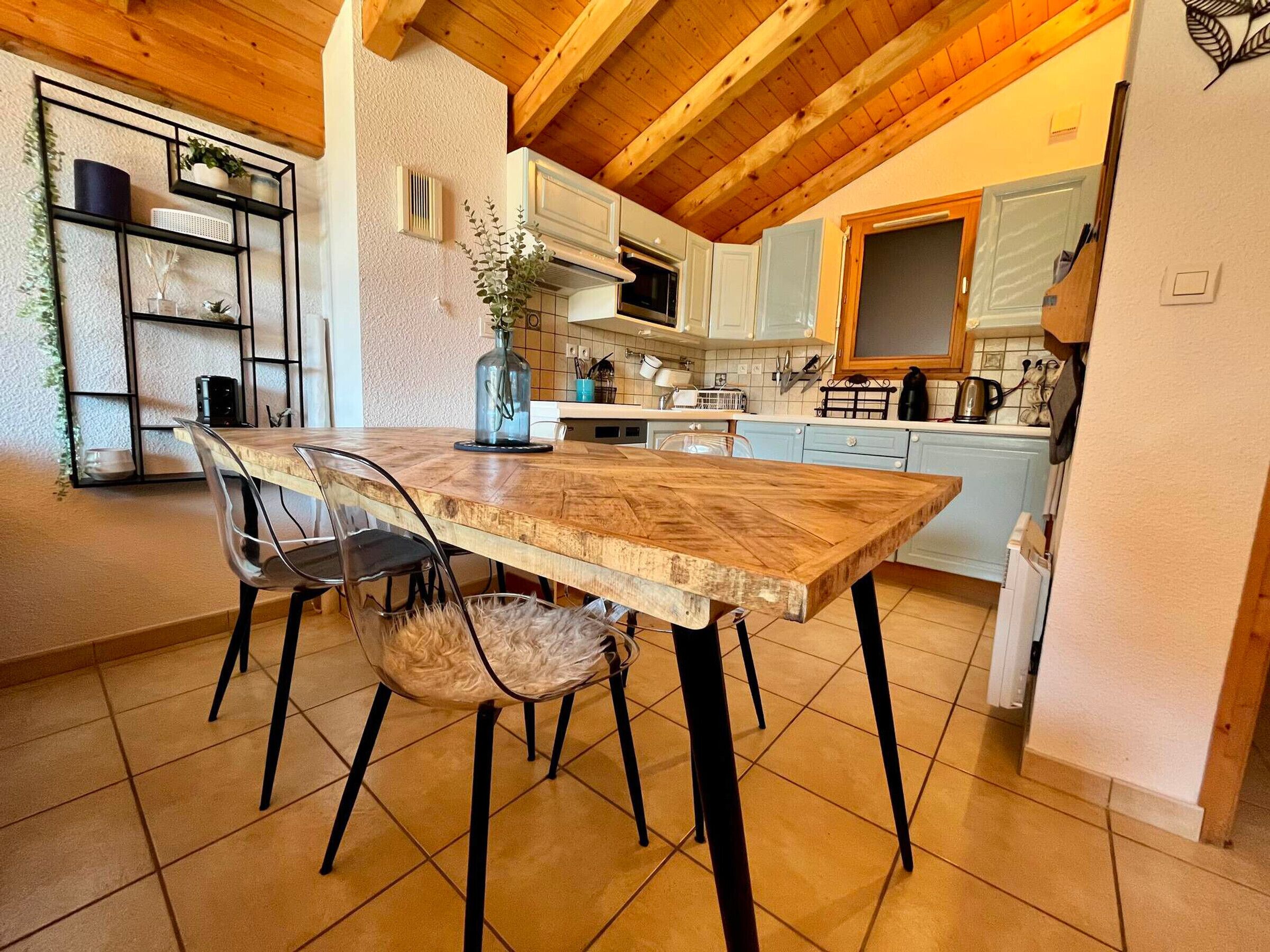 Una cucina con tavolo e sedie di legno, mobili bianchi e una pianta pensile.