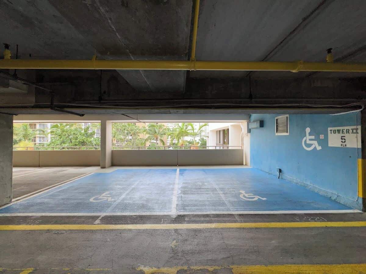 Un parking avec des places de stationnement bleues réservées aux personnes handicapées et un panneau indiquant « Tour 5, étage ».