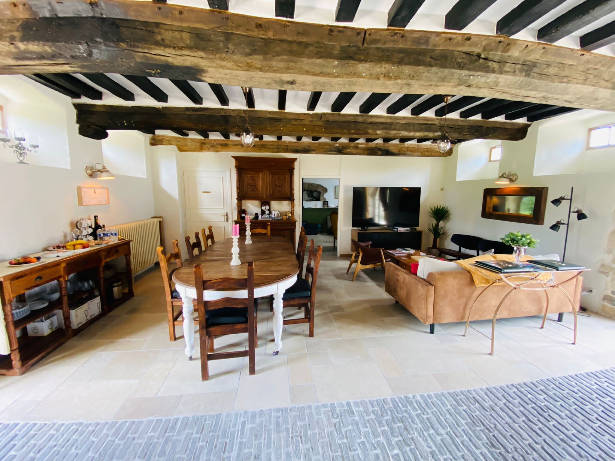A spacious living area with a dining table and chairs, a sofa, a TV, and a kitchen in the background.