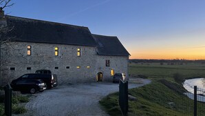 Un bâtiment en pierre avec une allée gravillonnée et des voitures garées.