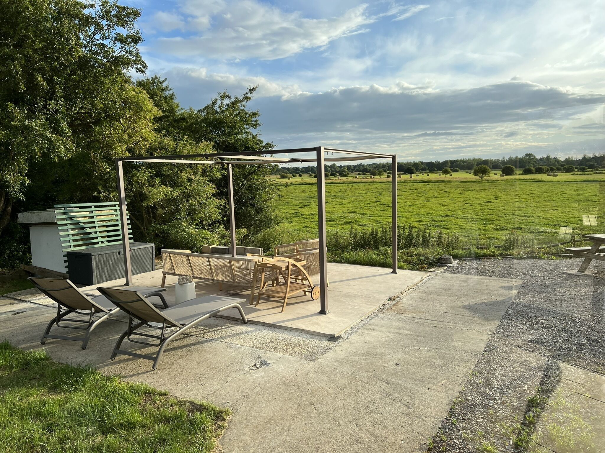 Un patio exterior con una pérgola, asientos y vistas a un campo verde.