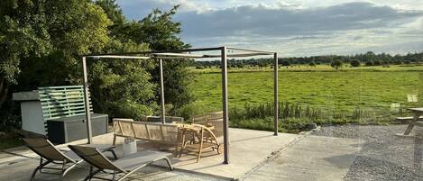 Un patio exterior con una pérgola, asientos y vistas a un campo verde.